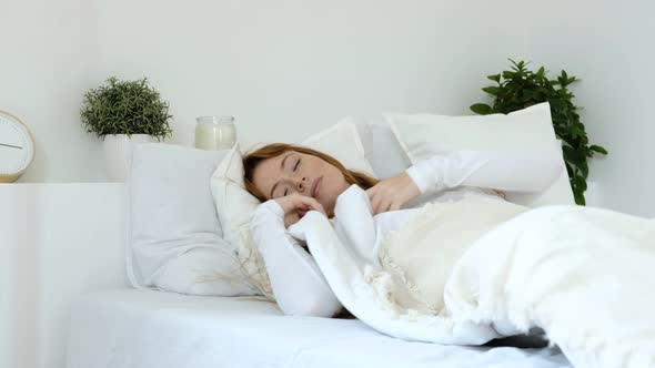 Young woman in bright white bedroom is lying in cozy bed
