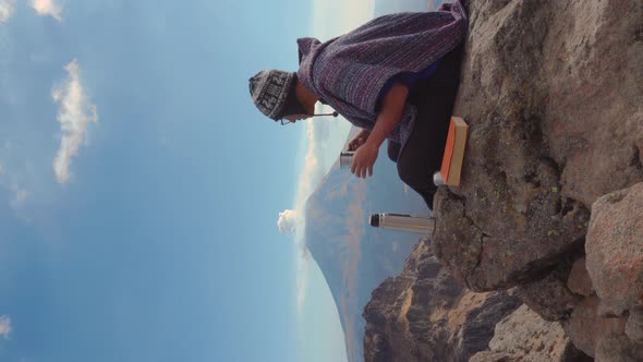 Man sitting outside on rocks  holding a book and looking the landscape alt