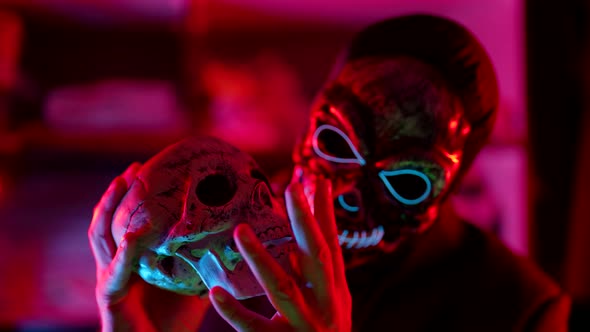 Mysterious Man with Skull Mask on Face is Holding Human Skull in Hands Black Magic alt