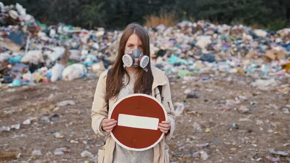 Portrait of Sad Young Woman in Gas Mask Holding Stop Sign While Standing in Toxic Smoke alt