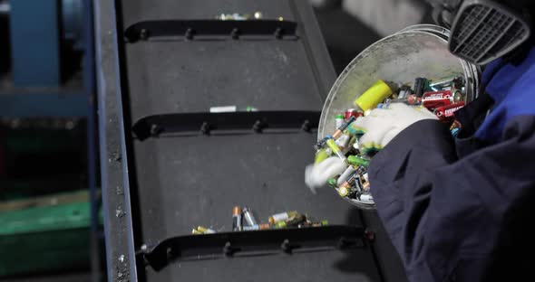 View of Hands of Person in Uniform and Gloves Pouring Out Used Batteries From Bucket Onto a Moving