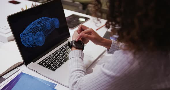 Creative businesswoman with laptop using smartwatch in modern office alt