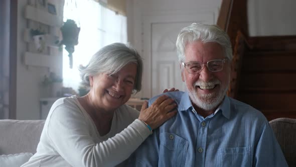 Portrait of couple of seniors laughing and having fun together sitting on the sofa of home alt