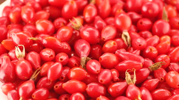 Close-up ripe rose hips are rotating. A bunch of rose hips on a plate. alt