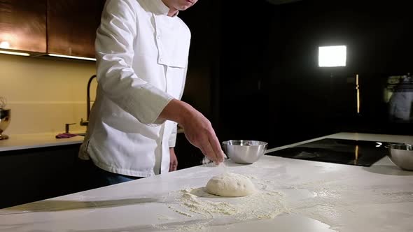 Baker in bakery makes morning dough for baking pizza sprinkles flour on dough