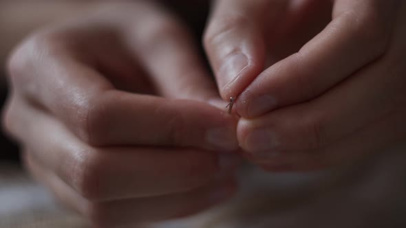 Close-up view of female hands inserting a thread into a needle hole for sewing. Handmade needlework. alt