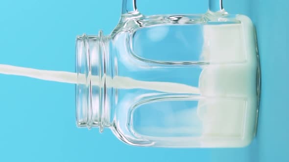 Vertical Video Slow Motion Closeup Shot of Milk Cold Beverage Drink Pooring Into Glass Jar Blue