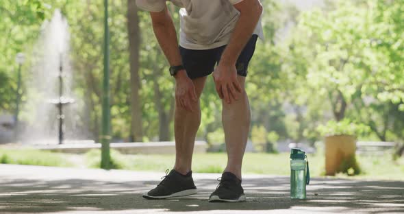 Senior man in pain holding his leg in the park alt