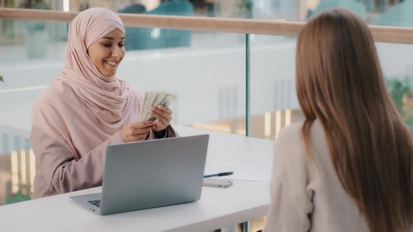 Young Friendly Smiling Arab Woman Manager Sits in Office at Desk Communicates with Client Explains alt