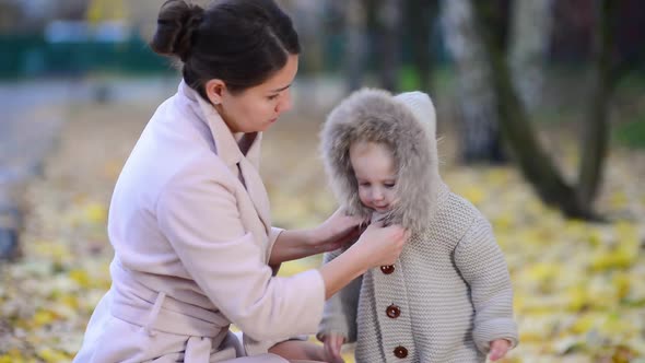 mother carefully fastens clothes to her little daughter on the street in the autumn evening alt