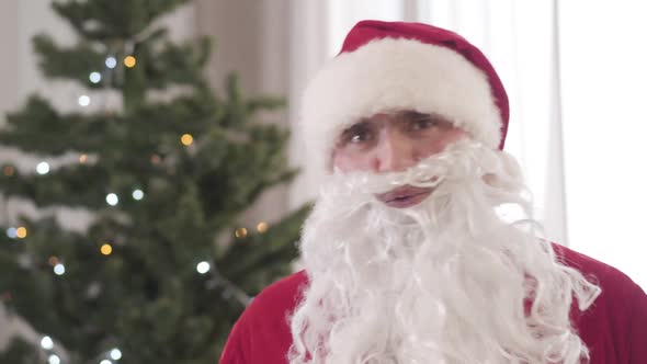 Close-up of Cheerful Young Caucasian Man in Red Santa Clause Costume and False Beard Dancing and alt