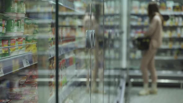 Young Woman Walking Down the Aisles of a Supermarket with a Basket of Groceries alt