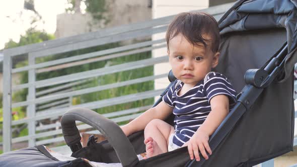 A Cute Baby 810 Months Old Sits in a Stroller Thinks About Something Stares at It After Which It