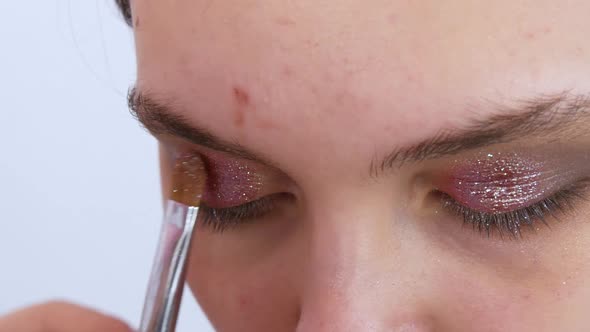 Professional Stylist Makeup Artist with a Brush Applies Shadows with Sparkles Making Bright Evening alt