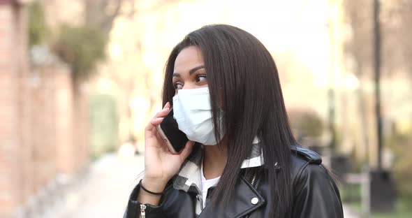 Beautiful black girl teenager wearing a face mask during COVID-19 and using phone.