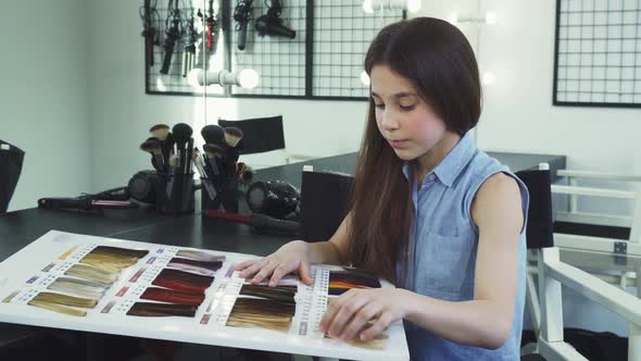 Pretty Little Girl Examining Hair Dye Color Chart at the Beauty Salon alt