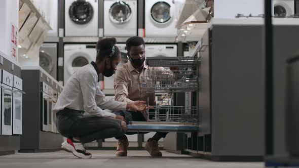 Afroamerican Married Couple with Face Masks are Choosing Dishwasher in Home Appliances Store alt