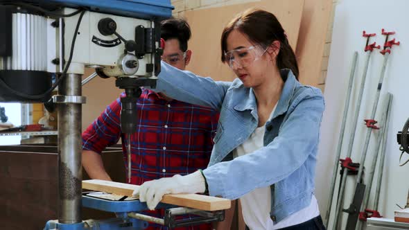 Asian Carpenter teaching woman student to use a drilling  machine in a university wood workshop
