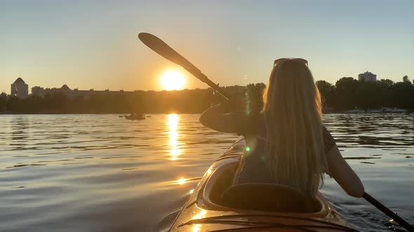 Young Woman Paddling on a Kayak Against Beautiful Orange Sunset alt