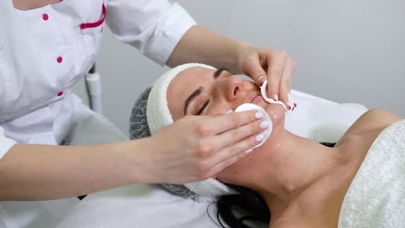 Beautician cleansing face of woman in beauty salon alt