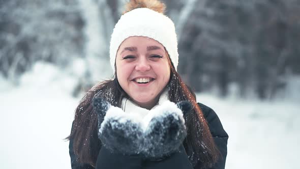 A Young Girl in a White Hat Blowing a Handful of Snow on Camera alt