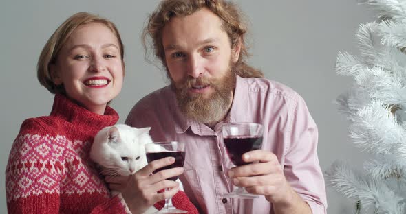 Portrait of Bearded Man Hugs His Blonde Wife with Short Hair in Red Sweater Holds Glass of Wine in alt