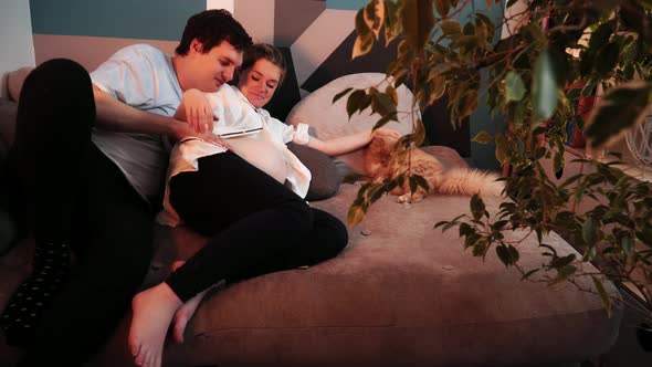 Pregnant Woman Laying in Her Husband's Embrace and He Kisses Her alt