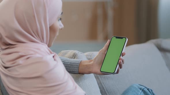 Over Shoulder Business Woman Islamic Arabian Girl in Hijab Sit on Cozy Sofa at Home Hold Mobile in alt