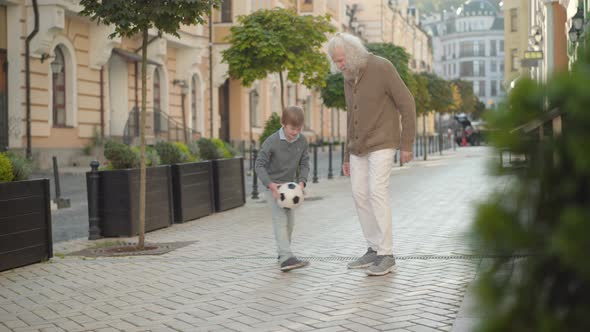Happy Little Boy Running with Soccer Ball To Smiling Senior Man. Joyful Caucasian Grandson and alt