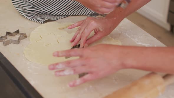 Mid section of mother and daughter cutting the dough with baking tin in star shapes in the kitchen alt
