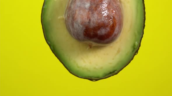 Water drops falling from avocado on yellow background. Avocado slice and water splashing, drops alt