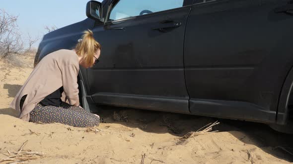 Young Woman Sits on Knees Remove Sand From Under Car alt