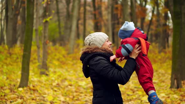 Young woman and boy 2 years have fun in the autumn park. Mom holds his son by the hands