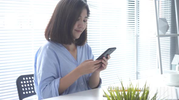 Beautiful young smiling asian woman working on laptop while sitting in a living room at home. alt