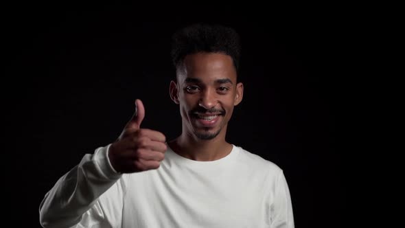 Handsome Man on Black Studio Background Smiles to Camera and Gives Thumbs Up.  alt