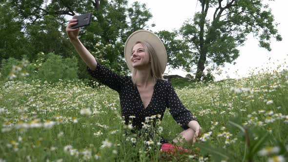 Blonde girl in dark dress in a chamomiles flowers meadow take a selfie