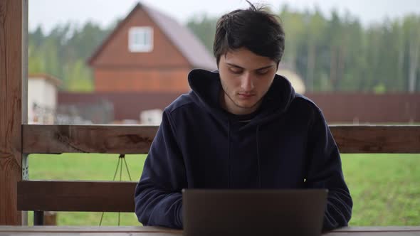 A Young Man is Typing on a Laptop While Sitting on a Terrace Against the Backdrop of a Picturesque alt