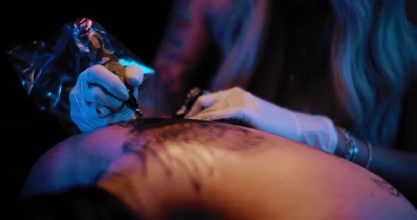 Close up of tattoo artist's hand making a big tattoo drawing on a person's back alt