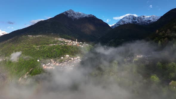 Flight through clouds with scenic view of Italian alp village in hillside; drone alt