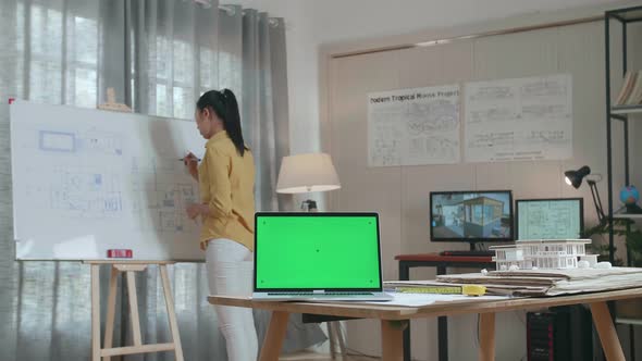 Asian Woman Engineer With Green Screen Laptop Drawing Blueprint On The Whiteboard At The Office alt