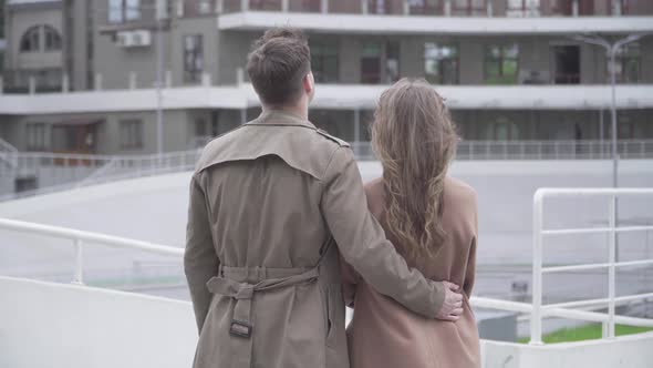 Back View of Young Caucasian Couple Hugging in Front of Skyscraper. Loving Boyfriend and Girlfriend alt