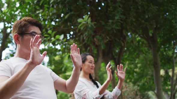 Happy asian couple exercising in garden with daughter, practicing tai chi together alt