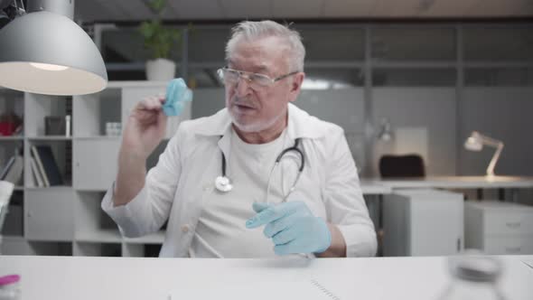 A Tired Elderly Experienced Doctor Nervously Removes His Latex Gloves After a Hard Days Work alt