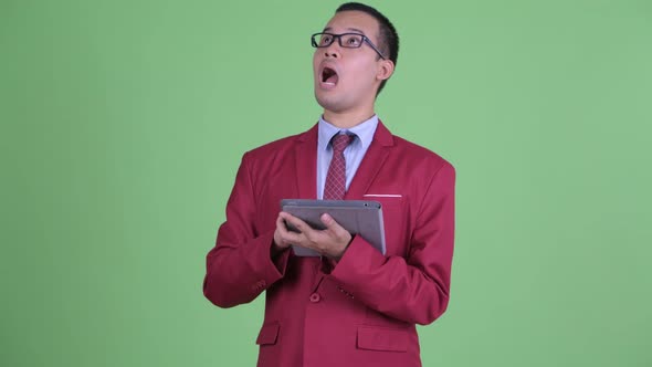 Happy Asian Businessman Thinking While Using Digital Tablet alt