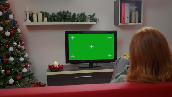 A girl watching Green Screen Mockup TV in a Chrismas decorated living room. alt