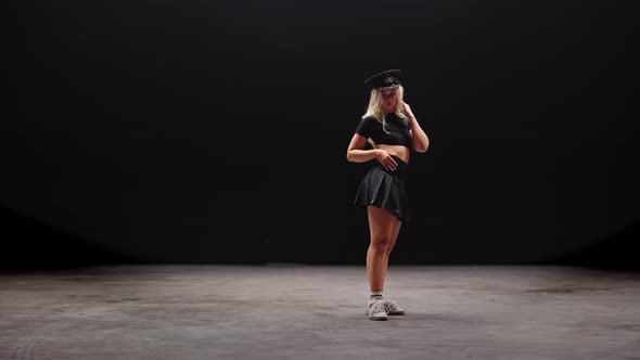 Young Woman in Policemans Hat Dances in Studio Against Black Background alt