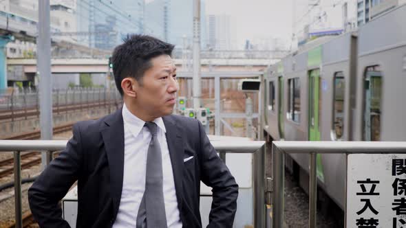Japanese businessman waiting on a train platform alt