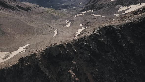 Aerial Flight Above Man Hiking Along Rocky Trail Path Close to Big Cliff in a Mountains