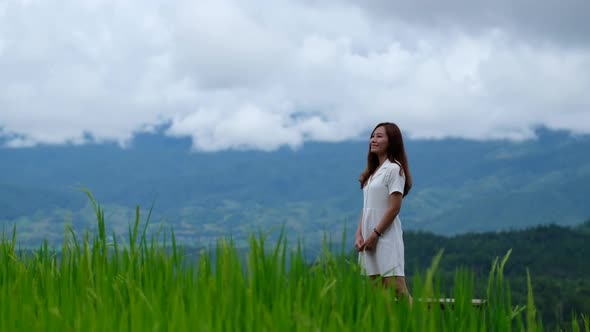 A beautiful young asian woman in paddy field with mountains and cloudy sky background