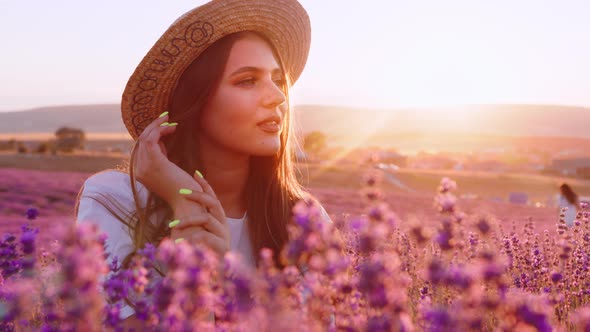 Beautiful Young Girl in a Straw Hat and White Dress Sitting in a Lavender Field on Sunset